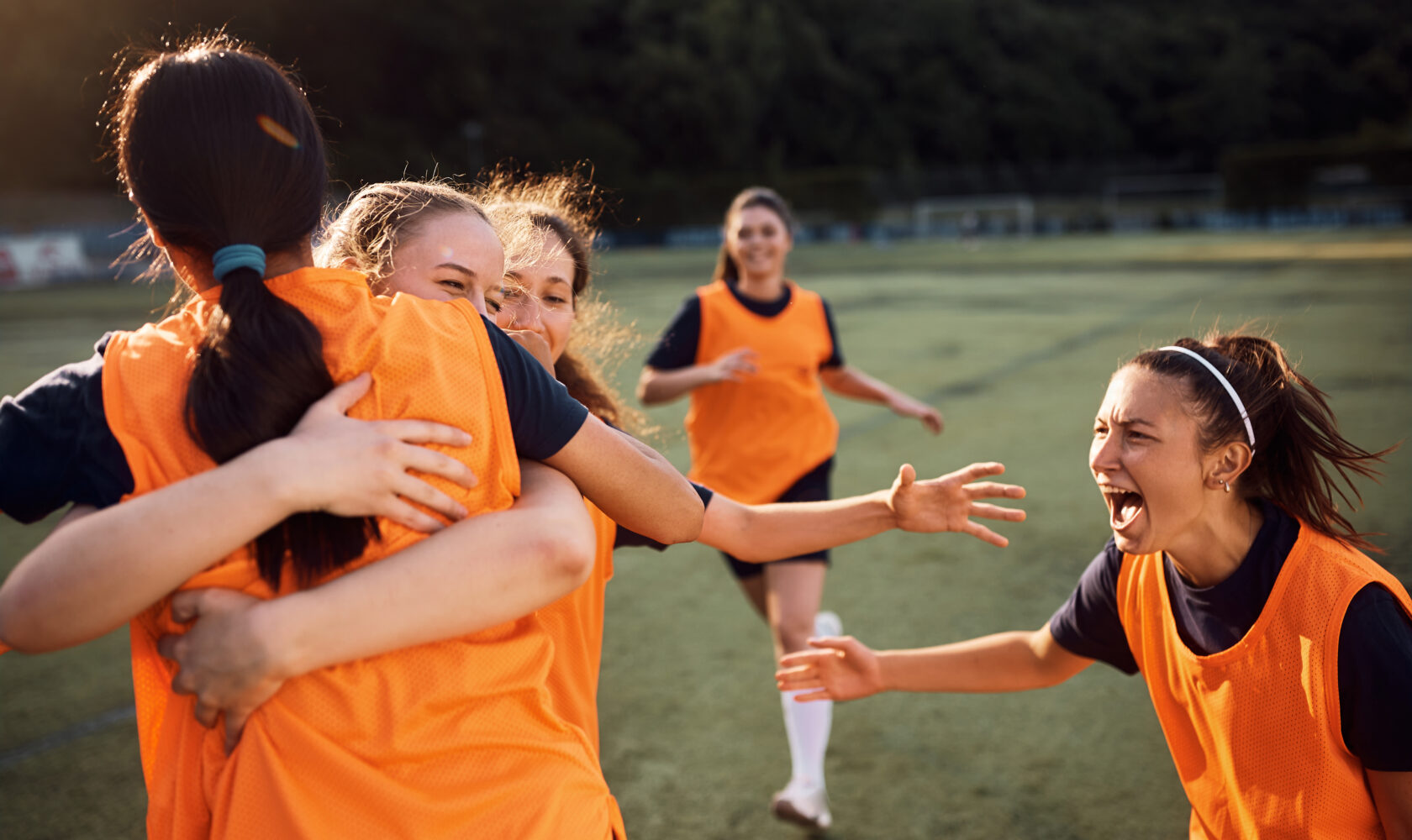 A group of girls celebrating and hugging on a football field.